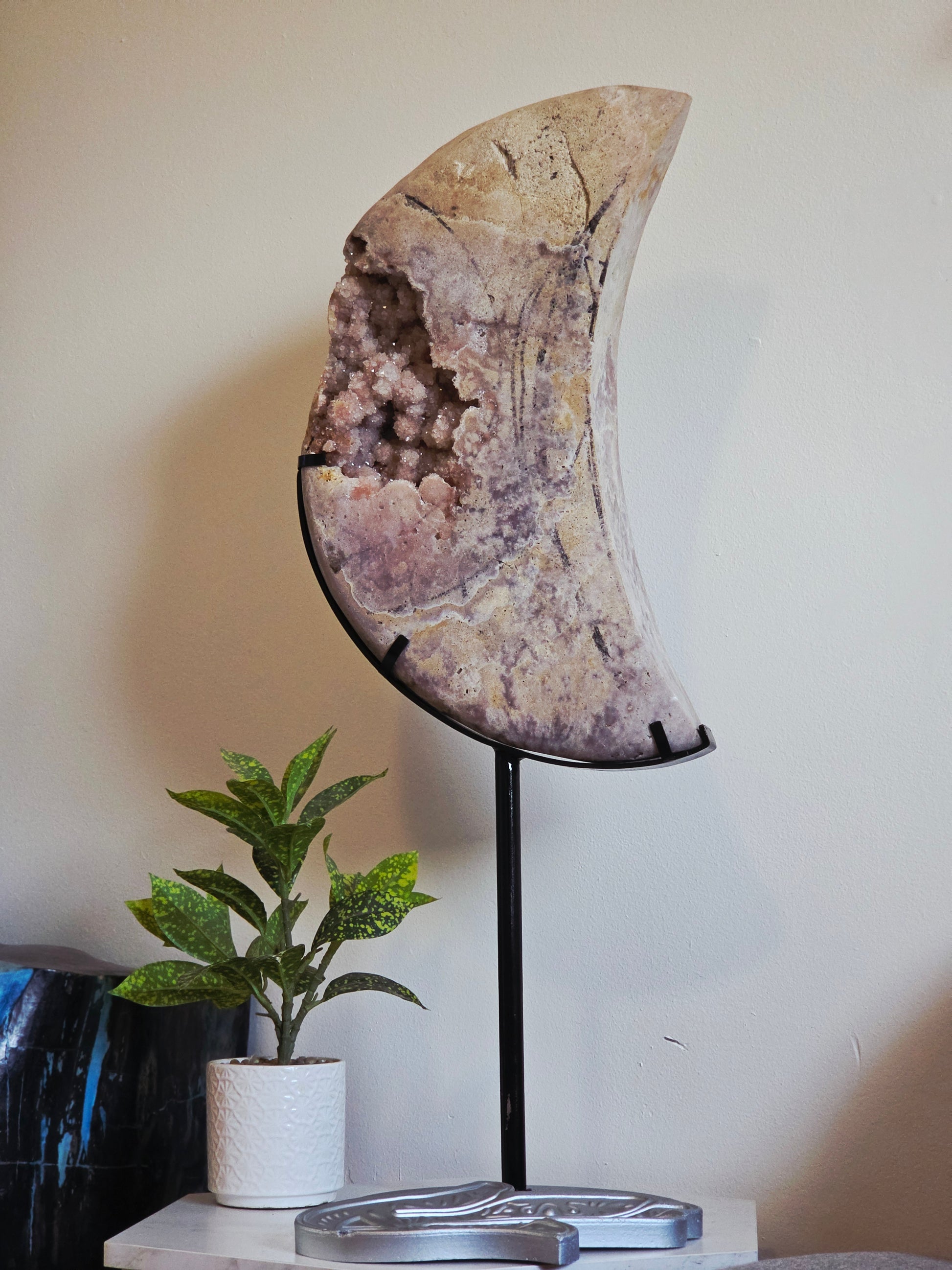 Large Pink Amethyst crescent moon carving with sparkling druzy crystals on a black metal stand.